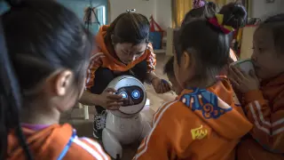 Los pequeños de una guardería China, junto al robot que les da clase
