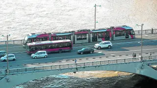 Un autobús y un tranvía recorren en paralelo el puente de Santiago.