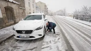 Un hombre pone cadenas a su coche en Cedrillas (Teruel) que se encuentra cubierta por la nieve caída en las últimas horas.