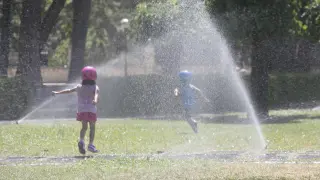 Dos niños combaten el calor refrescándose en el Parque Grande de Zaragoza