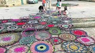 Los vecinos de Perales extienden el gran tapiz tejido por ellos para colgarlo en la plaza del pueblo.