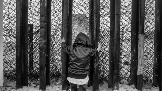Un niño se agarra a los barrotes del muro fronterizo en la playa de Tijuana