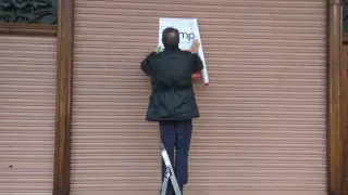Un empleado de la inmobiliaria, colgando el cartel en el que se anuncia la venta del local de Casa Gavín.