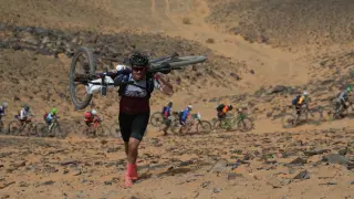 Un ciclista, con la bicicleta a hombros, sube una duna en la Titan Desert 2019.