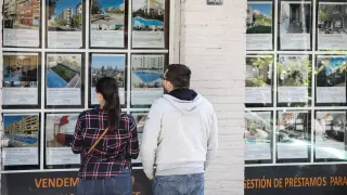 Una pareja mira anuncios de pisos en una inmobiliaria.