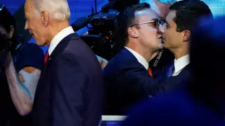 Pete Buttigieg recibe un beso de su marido Chasten con Joe Biden en primer término