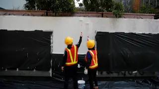 Dos trabajadores adecentan una fachada con pintadas tras una manifestación en Hong Kong