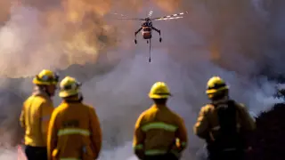Varios bomberos miran cómo un helicóptero arroja agua sobre el incendio Getty.