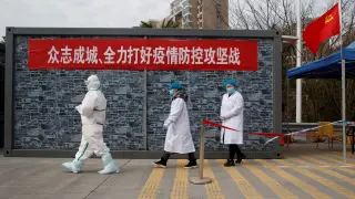 Personal de un hospital con ropa protectora camina hacia un punto de control en la zona de exclusión de la provincia china de Hubei