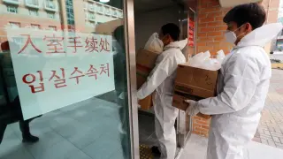 Empleados de la Universidad Nacional de Chunnam en Gwangju (Corea del Sur) se protegen para entregar comida a un grupo de estudiantes chinos que fueron aislados por el coronavirus