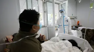 Un profesional sanitario con el traje de seguridad interactúa con un paciente en una habitación de aislamiento de un hospital en Wuhan.