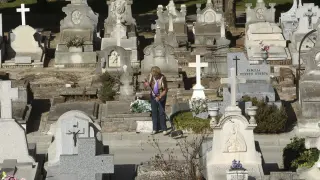 Una mujer limpia la lápida de una tumba en el cementerio de La Almudena.