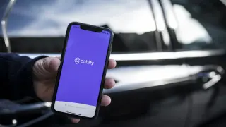 Un móvil con la aplicación de Cabify junto a uno de los coches que comenzarán a circular este miércoles en Zaragoza.