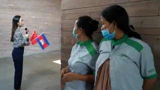 Airport cleaners in face masks observe a Cambodian TV reporter as a plane arrives from China to Cambodia with supplies and doctors donated to contain the spread of the coronavirus disease (COVID-19) outbreak