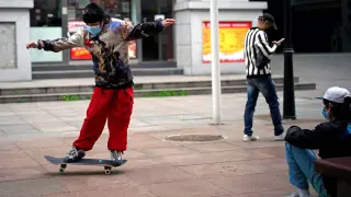 Un joven con mascarilla juega con un monopatín en Wuhan.