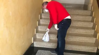 Un voluntario deposita una bolsa de medicamentos en las escaleras de acceso a una vivienda