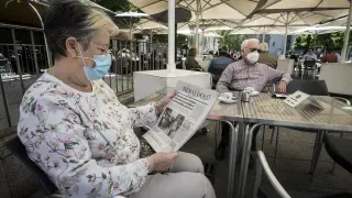 Una mujer con mascarilla leyendo HERALDO DE ARAGÓN en una terraza de Zaragoza