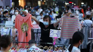 Vendor holds clothing items for sale at a street stall on Jianghan Road in Wuhan