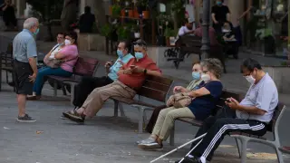 Personas con mascarilla sentadas en un banco en Barcelona.