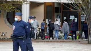 Varias personas depositan flores en la entrada del colegio donde daba clase el profesor asesinado.