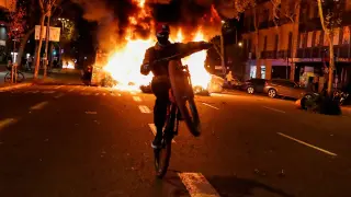 Un joven con una moto pasa junto a una barricada ardiendo en Barcelona