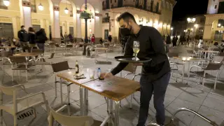 Un camarero limpia las últimas mesas para cerrar a las 20.00 en la plaza de López Allué de Huesca.