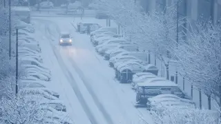 Un coche circula por una calle nevada de Zaragoza.