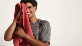 Young attractive black sportsman laughs and wipes his face with a red towel, right half of the face open, against white background