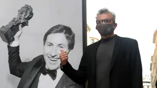 El presidente de la Academia de Cine, Mariano Barroso, junto a una foto de una exposición en Málaga que celebra la gala de los Goya.