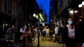 FILE PHOTO: People wearing protective masks walk past bar customers after bars reopened in Spain's Basque Country, amid the coronavirus disease (COVID-19) outbreak, in Bilbao