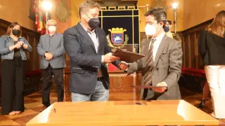 El alcalde de Huesca (d) y el consejero de Vertebración del Territorio, Movilidad y Vivienda, intercambian los documentos del convenio tras la firma del convenio.