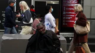 A woman sits between sidewalk barriers amid the coronavirus disease (COVID-19) pandemic, as others pass in the Midtown Manhattan area of New York City