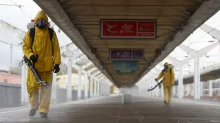 Dos operarios con trajes de protección desinfectan una estación de tren en Moscú