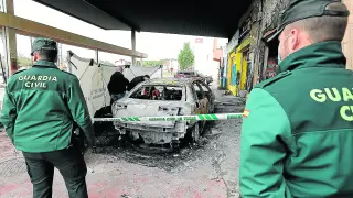 Dos guardias civiles custodian el coche consumido por las llamas en la gasolinera de Mora de Rubielos.