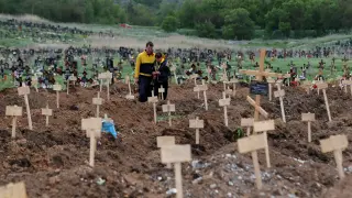 Dos personas visitan una tumba en un cementerio improvisado en Mariúpol.