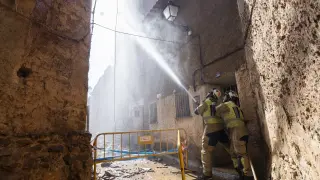 Bomberos echando agua en el casco urbano de Moros después del paso del fuego.