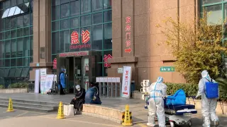 Trabajadores con trajes protectores empujan una cama de hospital fuera del Hospital Central de Wuhan