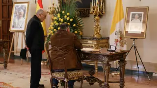 Dos hombres firman el libro de condolencias de Benedicto XVI en la Nunciatura de España.