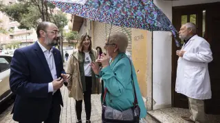 Javier Lambán y Lola Ranera hablan con una vecina de Las Fuentes que se protege de la tímida lluvia
