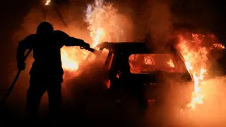 Un bombero apaga un vehículo en llamas en un suburbio de París