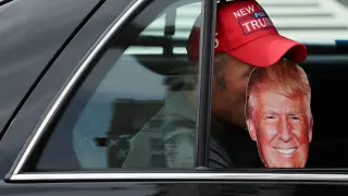 Una persona sostiene una máscara de Donald Trump dentro de un vehículo.