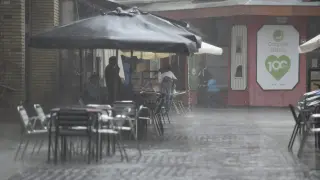 Varias personas se protege de la lluvia en una terraza en Huesca.