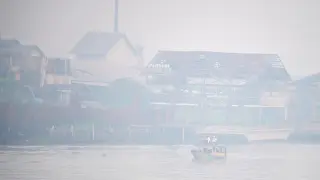 Estudiantes viajan en un bote de madera por el río Ogan, cubierto de niebla debido a los incendios forestales, en Indonesia