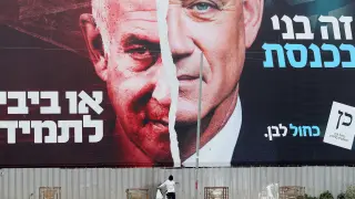 FILE PHOTO: A boy looks up at a Blue and White party election campaign banner depicting its leader, Israeli Defence Minister Benny Gantz, alongside Israeli Prime Minister Benjamin Netanyahu, ahead of the March 23 ballot, in Bnei Brak, Israel March 22, 2021. REUTERS/Ammar Awad/File Photo