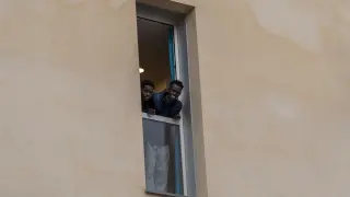Dos de los migrantes que se alojan en el albergue de Cella se muestran sonrientes desde una de las ventanas