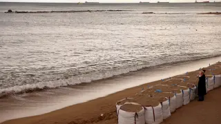 Un turista bebe junto a bolsas llenas de arena para proteger la terraza de un 'Chiringuito' en la playa de la Barceloneta.