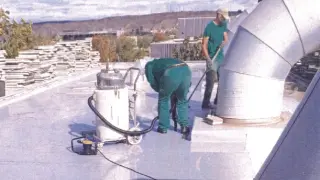 Dos obreros limpian el agua acumulada en el tejado de la comisaría del Actur tras una fuerte tormenta en octubre.