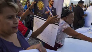 La gente recibe calendarios que muestran al presidente de El Salvador, Nayib Bukele, mientras sus partidarios hacen campaña para su reelección en San Salvador