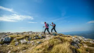 couple-hiking-nanos-plateau-slovenia-against-blue-sky
