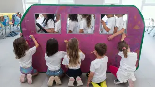 Un grupo de niños pinta una autocaravana en las colonias que por primera vez se celebran en el colegio Ana María Navales de Zaragoza